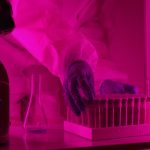 Cientista de jaleco manipula tubos de ensaio diante de um microscópio em um laboratório.