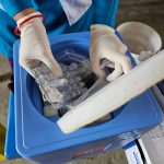 Profissional de saúde usando luvas manuseia frascos e amostras em um laboratório.