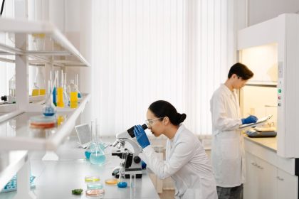 Dois pesquisadores trabalham com microscópios e tubos de ensaio em um laboratório equipado.