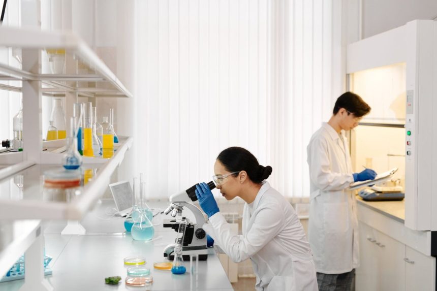 Dois pesquisadores trabalham com microscópios e tubos de ensaio em um laboratório equipado.