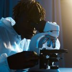 Cientista usando roupa de proteção examina amostras ao microscópio em um laboratório.