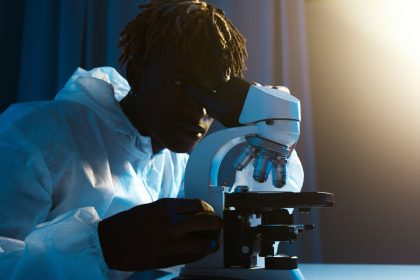 Cientista usando roupa de proteção examina amostras ao microscópio em um laboratório.