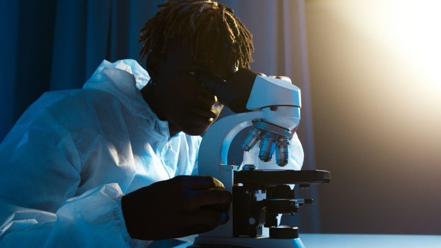 Cientista usando roupa de proteção examina amostras ao microscópio em um laboratório.