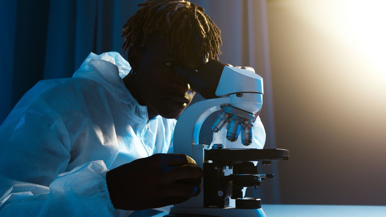 Cientista usando roupa de proteção examina amostras ao microscópio em um laboratório.