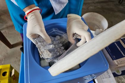 Profissional de saúde usando luvas manuseia frascos e amostras em um laboratório.