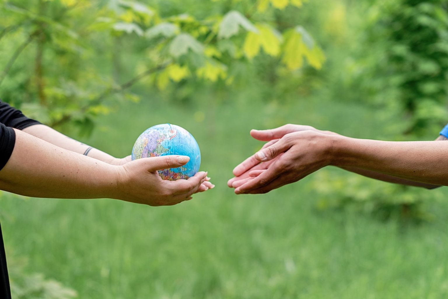 Duas mãos trocam um pequeno globo, simbolizando cooperação e união internacional.